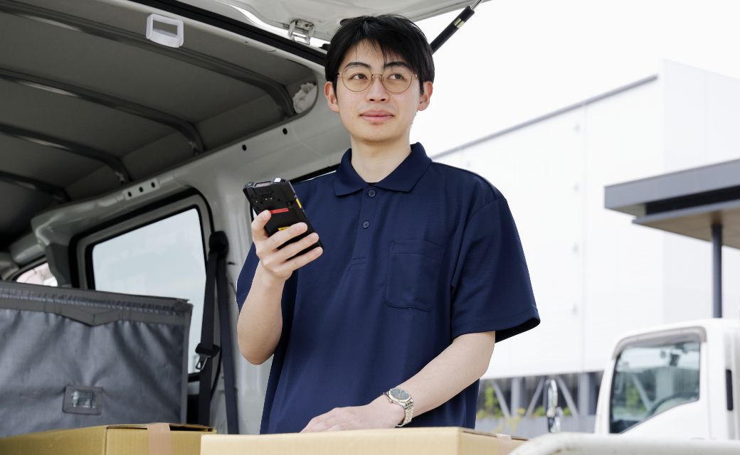 配送拠点にて、軽バンのバックドアを開け、端末を操作するS.S.さん
