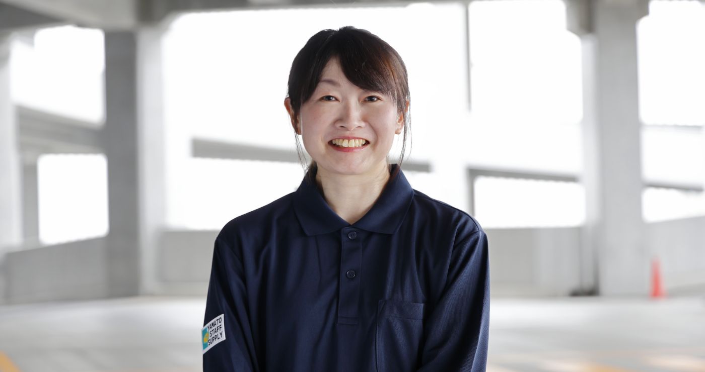 配送拠点の構内を背景に、柔和な笑顔でカメラを見つめるY.K.さん