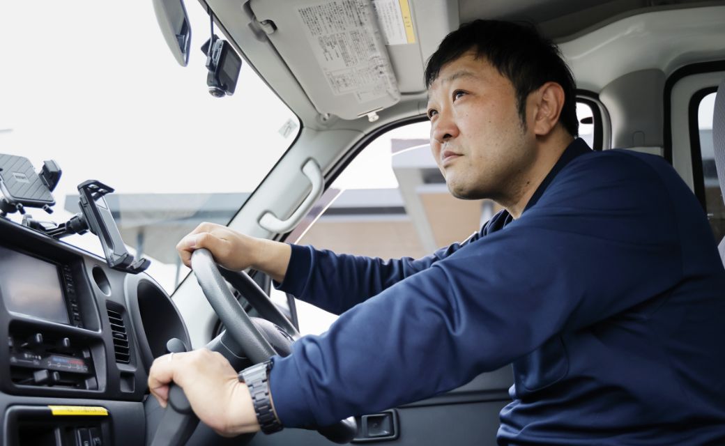 配送車両の運転席に座り、ハンドルを握って真剣な表情で前方を確認するA.H.さん