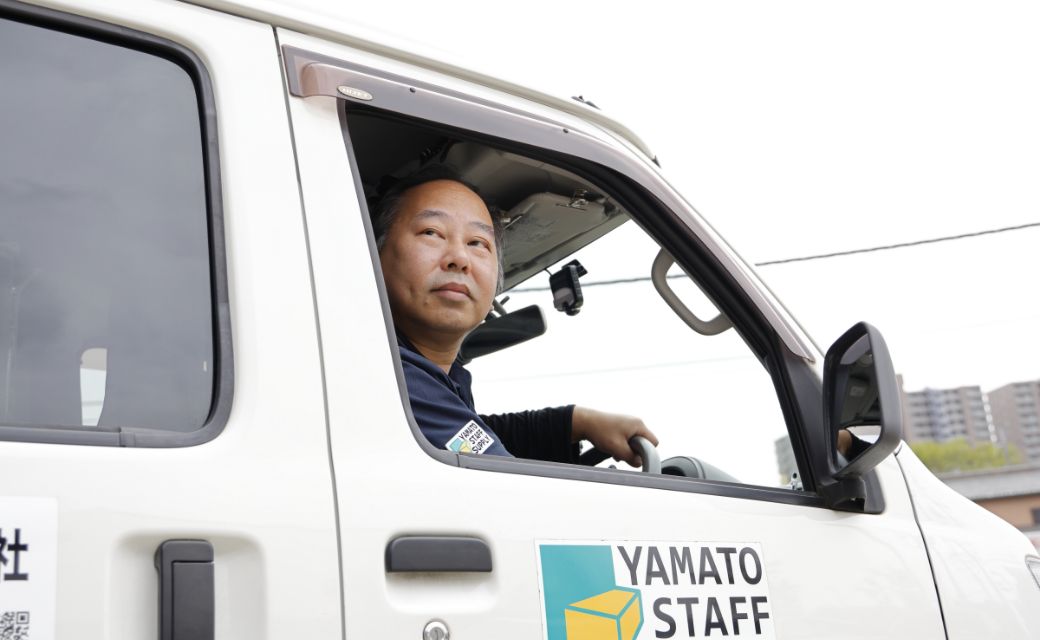 ヤマト・スタッフ・サプライのロゴが入った白い軽バンの運転席に座り、窓から穏やかかつ真剣な眼差しで前方を見つめるI.M.さん