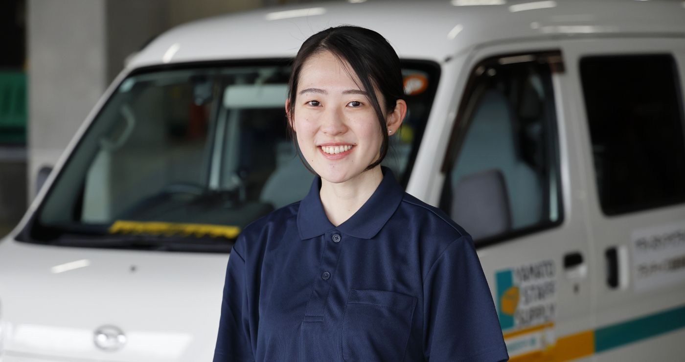 ヤマト・スタッフ・サプライの配送車両の前で、背筋を伸ばし晴れやかな表情で立つM.T.さん
