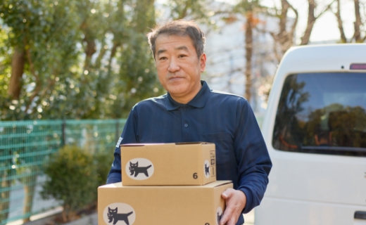 住宅街で配送車から荷物を降ろし、抱えて運んでいる様子